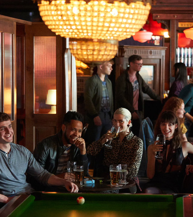 "Normal People - Verzeihen": Connell (Paul Mescal) und Marianne (Daisy Edgar-Jones) sitzen mit einigen anderen Personen in einer Bar und trinken etwas, während andere Billard spielen.