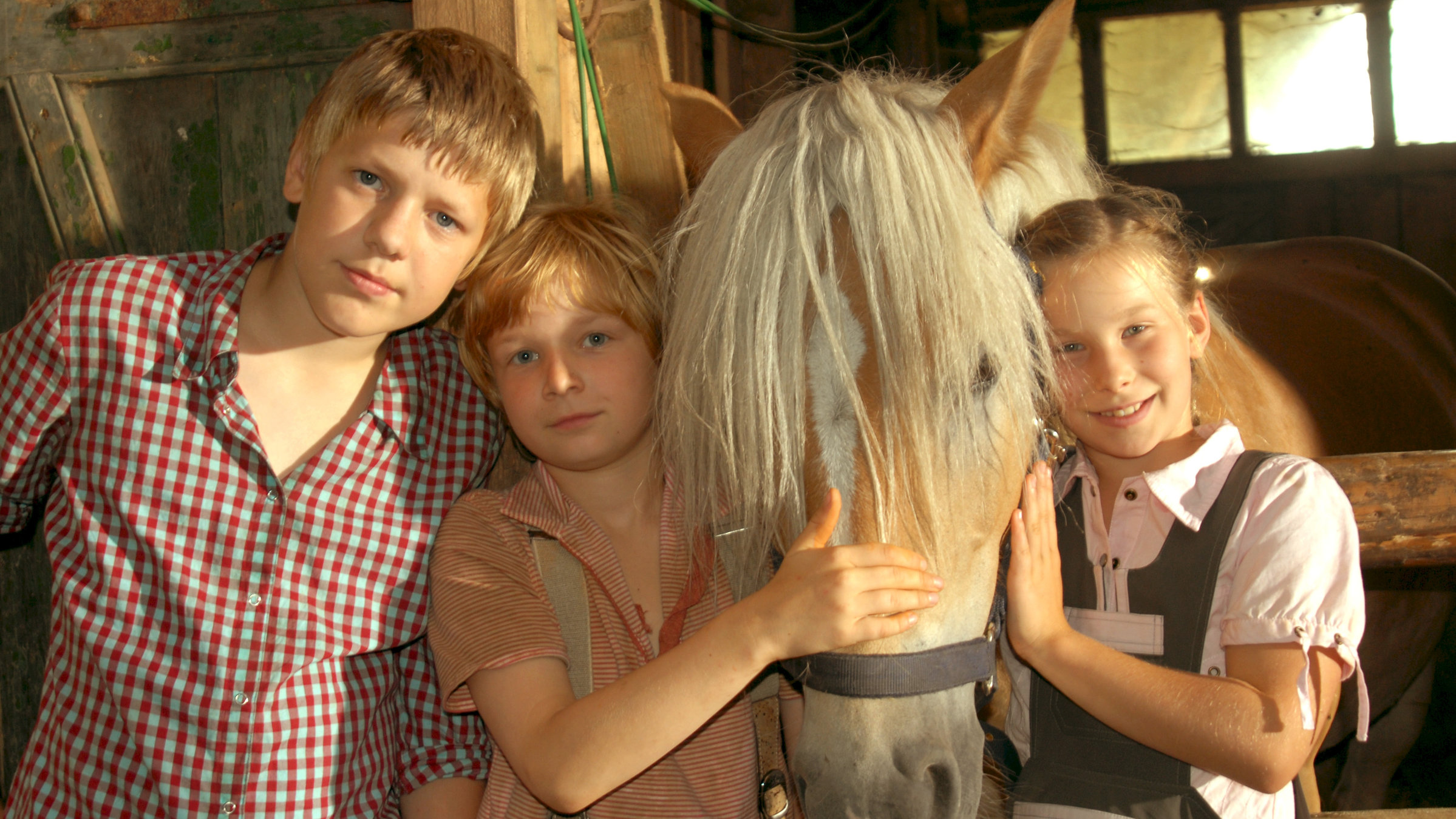 "Hände weg von Mississippi": Im Stall stehen Leo (Karl Alexander Seidel) und Emma (Zoë Charlotte Mannhardt) links und rechts neben dem Pferd Mississippi und streicheln dessen Kopf. Neben Leo steht sein Bruder Max (Konstantin Kaucher).