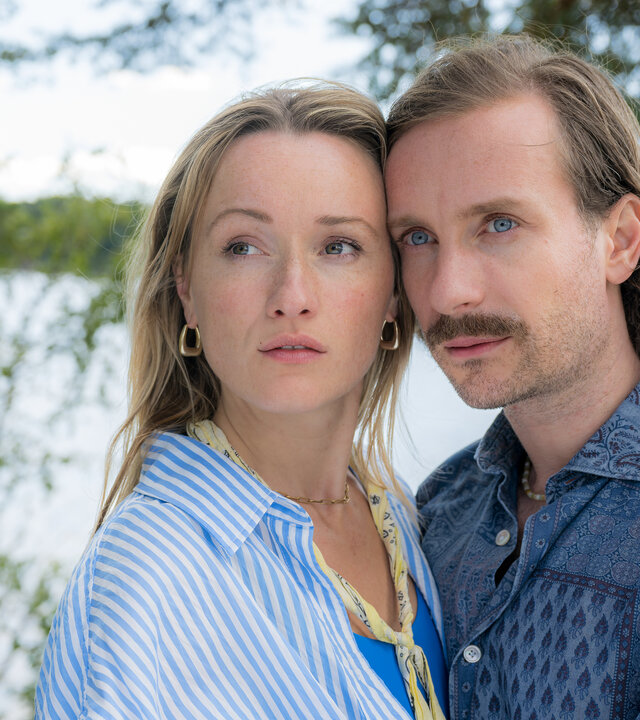 "Inga Lindström: Ein Sommer voller Wunder": Marie (Marie von Reibnitz) und Simon (Max Rothbart) stehen im Freien dicht beieinander Ihre Köpfe berühren sich seitlich, während sie gemeinsam auf einen Punkt in der Ferne sehen. Im Hintergrund liegt ein Ufer mit Gewässer.