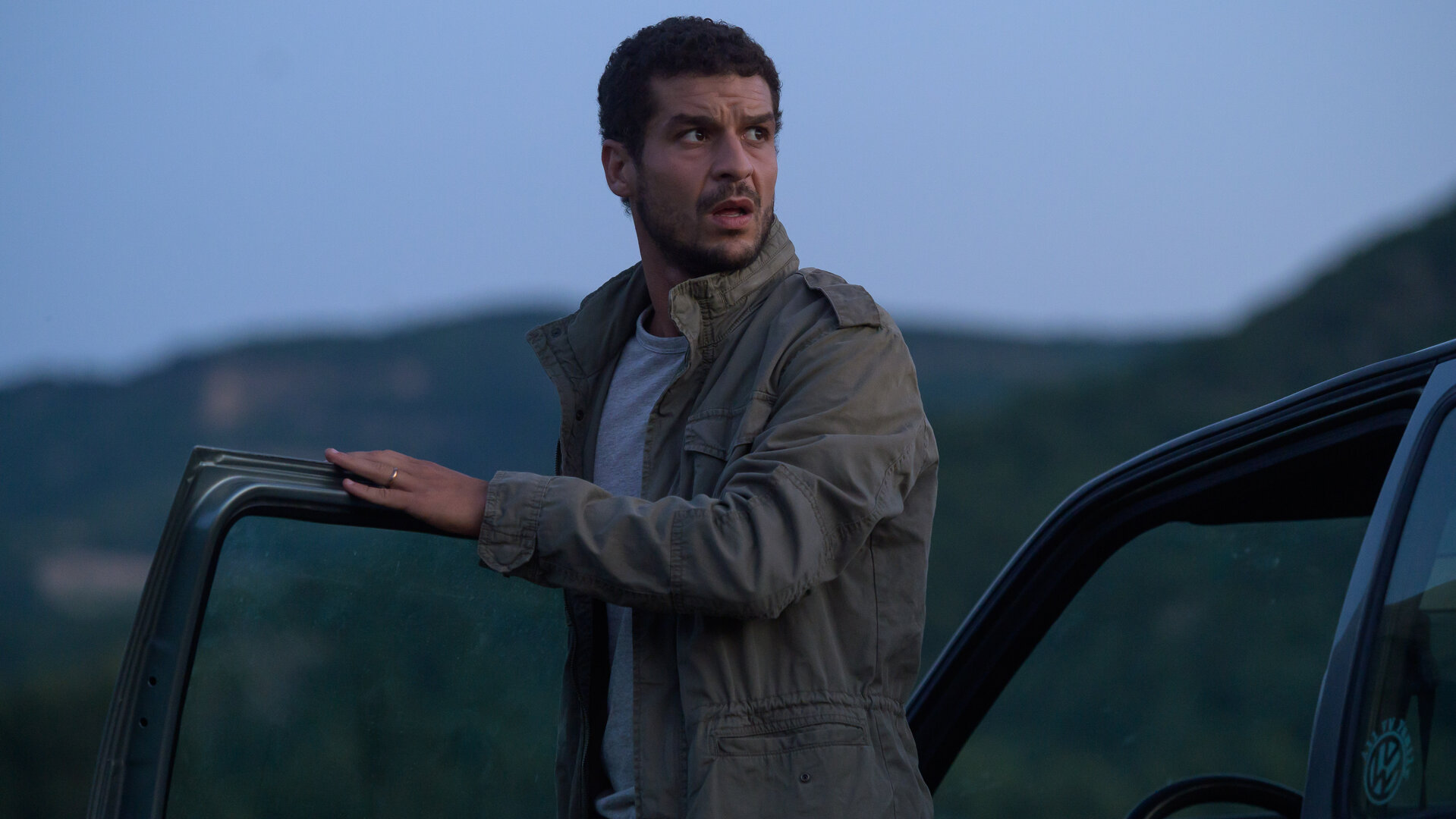 "Tödliche Ahnung - Blonde Besucherin": In der Abenddämmerung: Romain Sauvant (Soufiane Guerrab) ist aus dem Auto ausgestiegen und schaut sich suchend um.