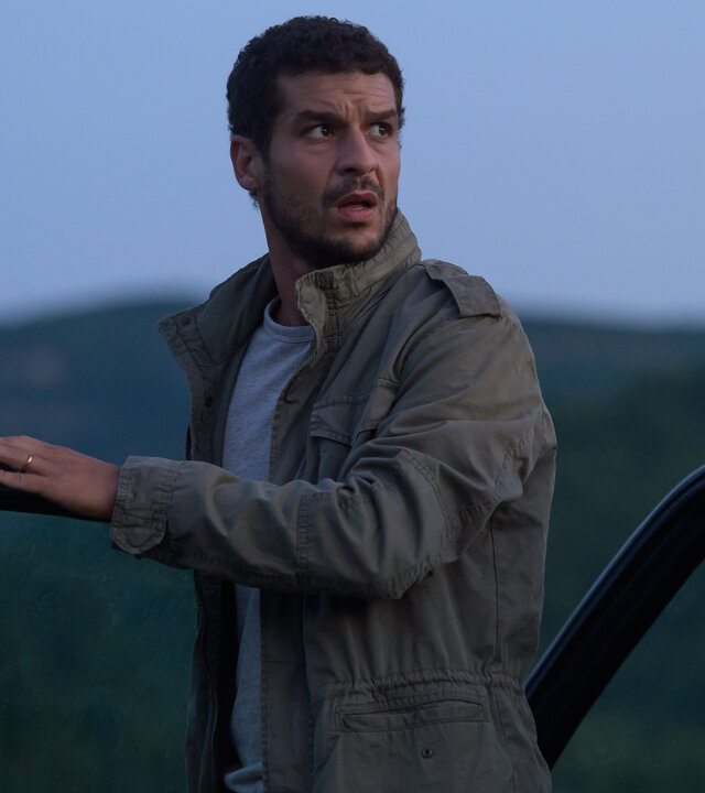 "Tödliche Ahnung - Blonde Besucherin": In der Abenddämmerung: Romain Sauvant (Soufiane Guerrab) ist aus dem Auto ausgestiegen und schaut sich suchend um.