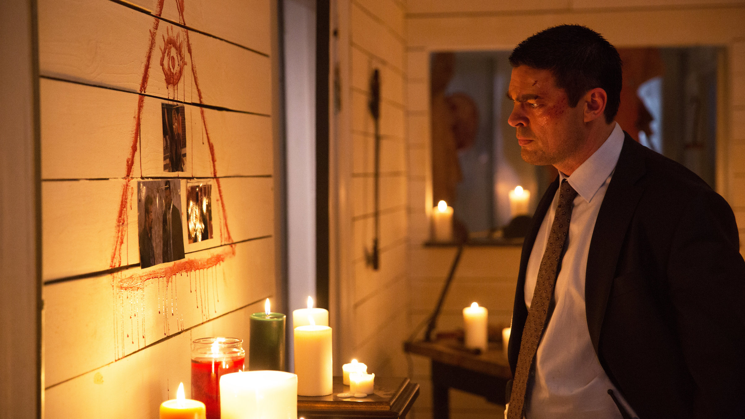 "Hangman - Spiel mit dem Tod": Detektiv Will Ruiney (Karl Urban) steht vor einer blutbeschmierten Wand, an der Fotos hÃ¤ngen. Im Raum brennt nur Kerzenlicht.