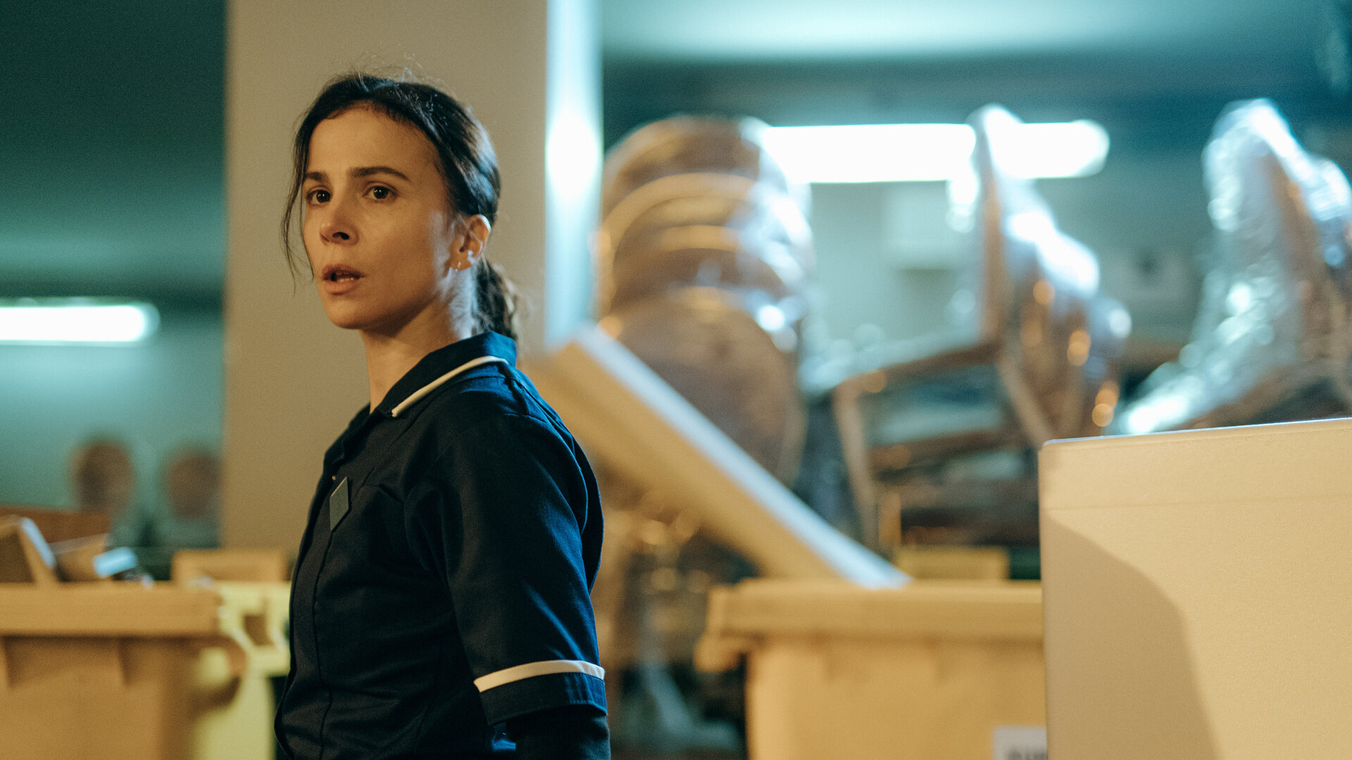 "Serial Cleaner - Die Mission": Teri Marquard (Aylin Tezel) steht in Arbeitskleidung in einem Lagerraum und schaut erstaunt zur Seite.