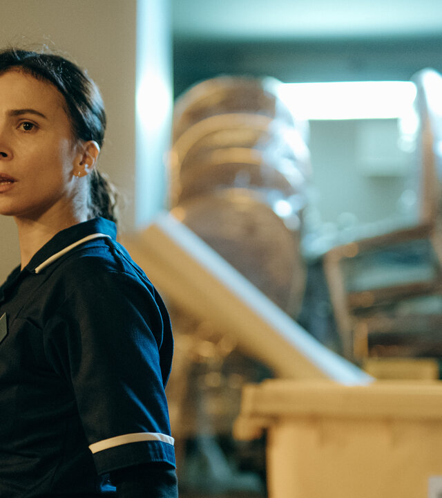 "Serial Cleaner - Die Mission": Teri Marquard (Aylin Tezel) steht in Arbeitskleidung in einem Lagerraum und schaut erstaunt zur Seite.