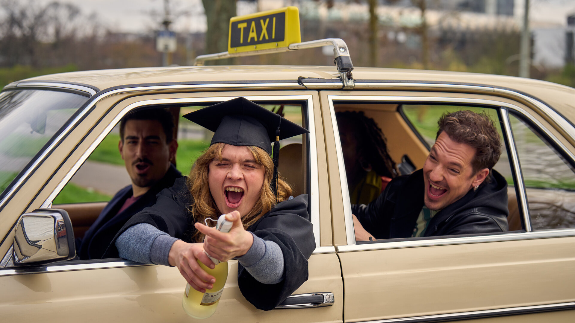 "BFF - Best Family Forever - SSW 19": Lena (Anna Schimrigk) sitzt mit ihren Freunden Flo (Anton Weil), Raúl (Nico Stank) und Nikita (Karmela Shako) in ihrem Taxi und öffnet eine Sektflasche. Alle lachen.