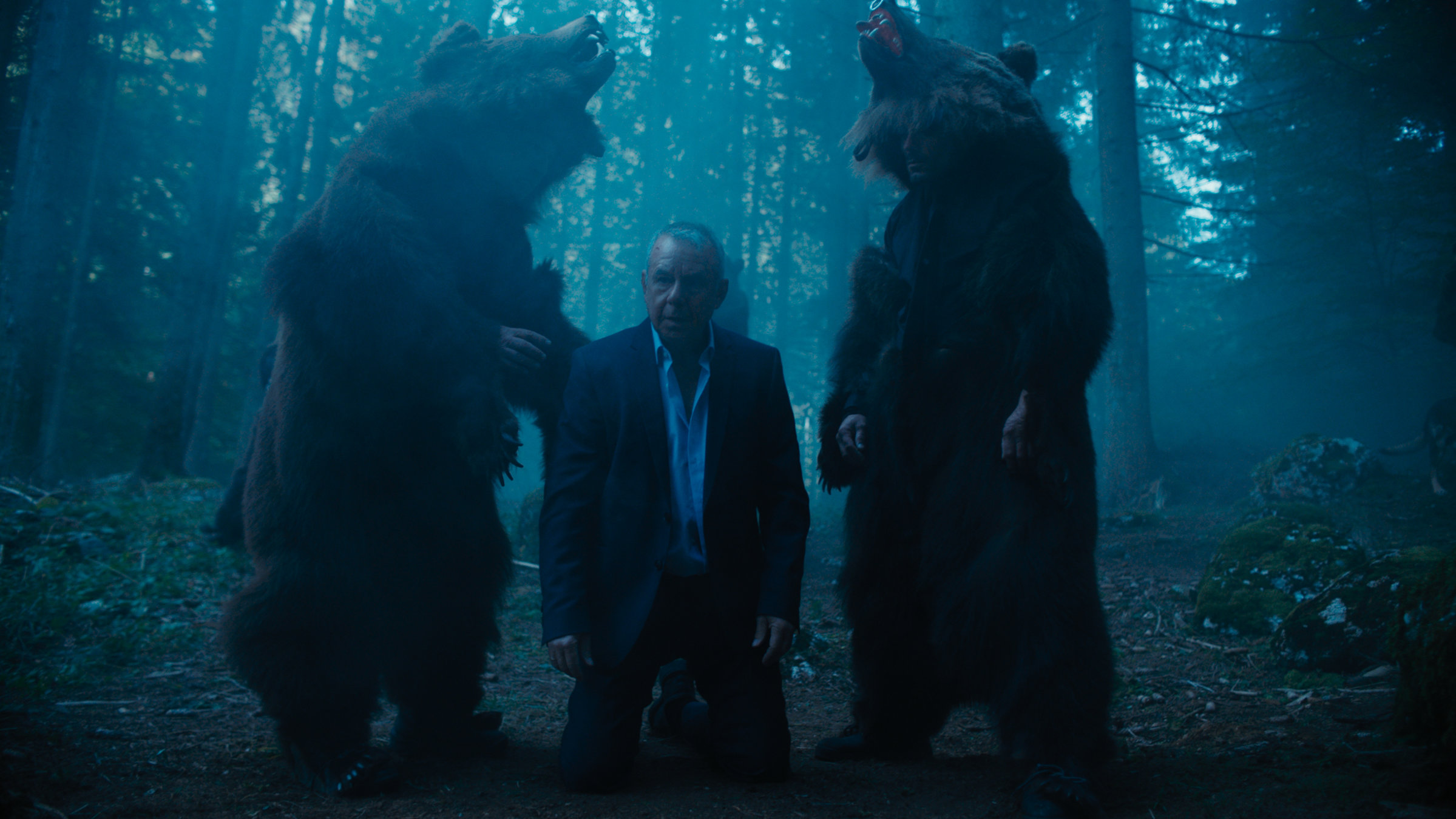 "Blutholz": Es ist Nacht in den rumänischen Wäldern. Hans Schüssler (Joachim Król) kniet zwischen zwei Menschen in Bärenkostümen.