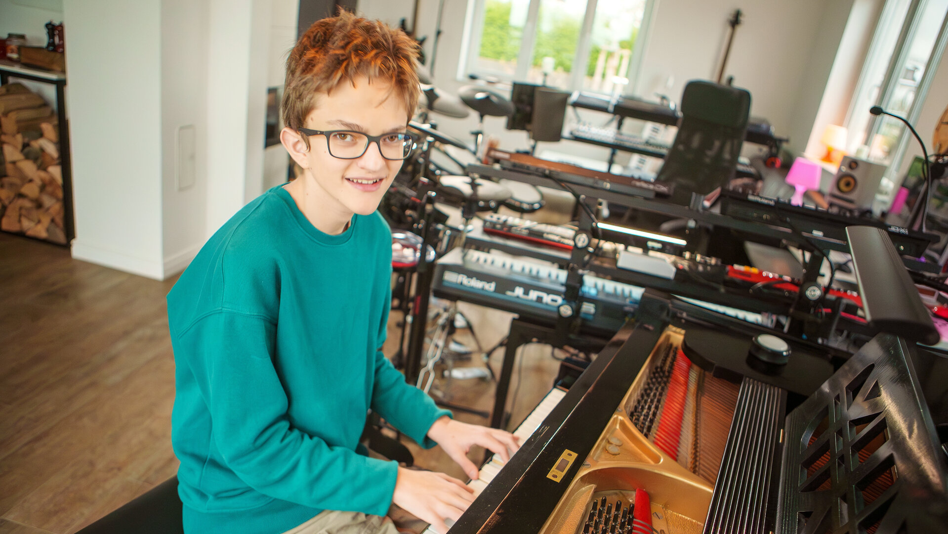 "einfach Mensch - Mika Mai: Musikgenie mit ASS": Mika Rocky Mai trägt eine Brille, die ihm hilft, seine Umgebung besser wahrzunehmen. Er sitzt zu Hause im Wohnzimmer am Konzertflügel und spielt Klavier.
