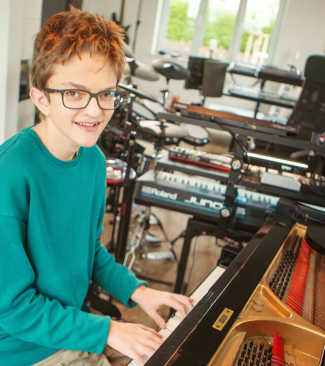 "einfach Mensch - Mika Mai: Musikgenie mit ASS": Mika Rocky Mai trägt eine Brille, die ihm hilft, seine Umgebung besser wahrzunehmen. Er sitzt zu Hause im Wohnzimmer am Konzertflügel und spielt Klavier.