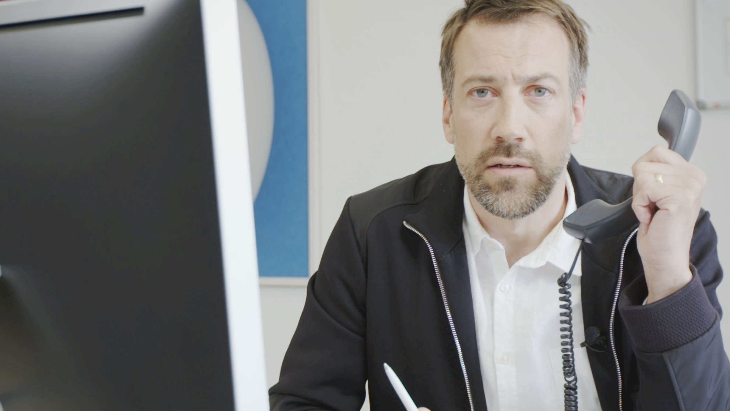 "ZDFzeit: Der große Warentest - Richtig sparen im Haushalt": Moderator Marcus Niehaves sitzt an einem Tisch und hält mit fragendem Gesichtsausdruck einen Telefonhörer in der Hand.