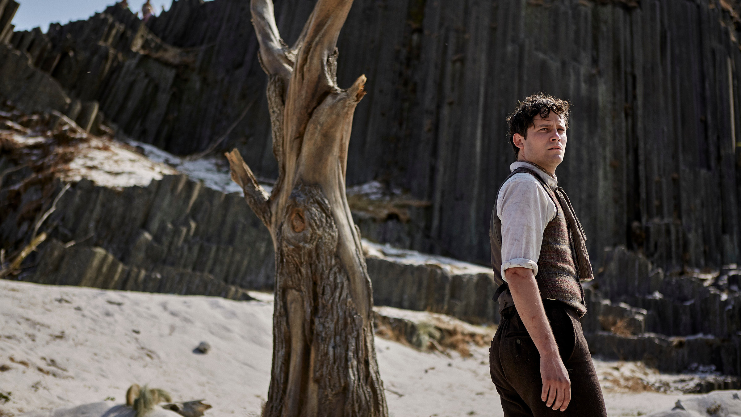 "Der Uhrmacherlehrling": Urban (Michael Balcar) in altmodischer Kleidung steht mit besorgter Miene auf einem Bergplateau neben einem abgestorbenen Baum.