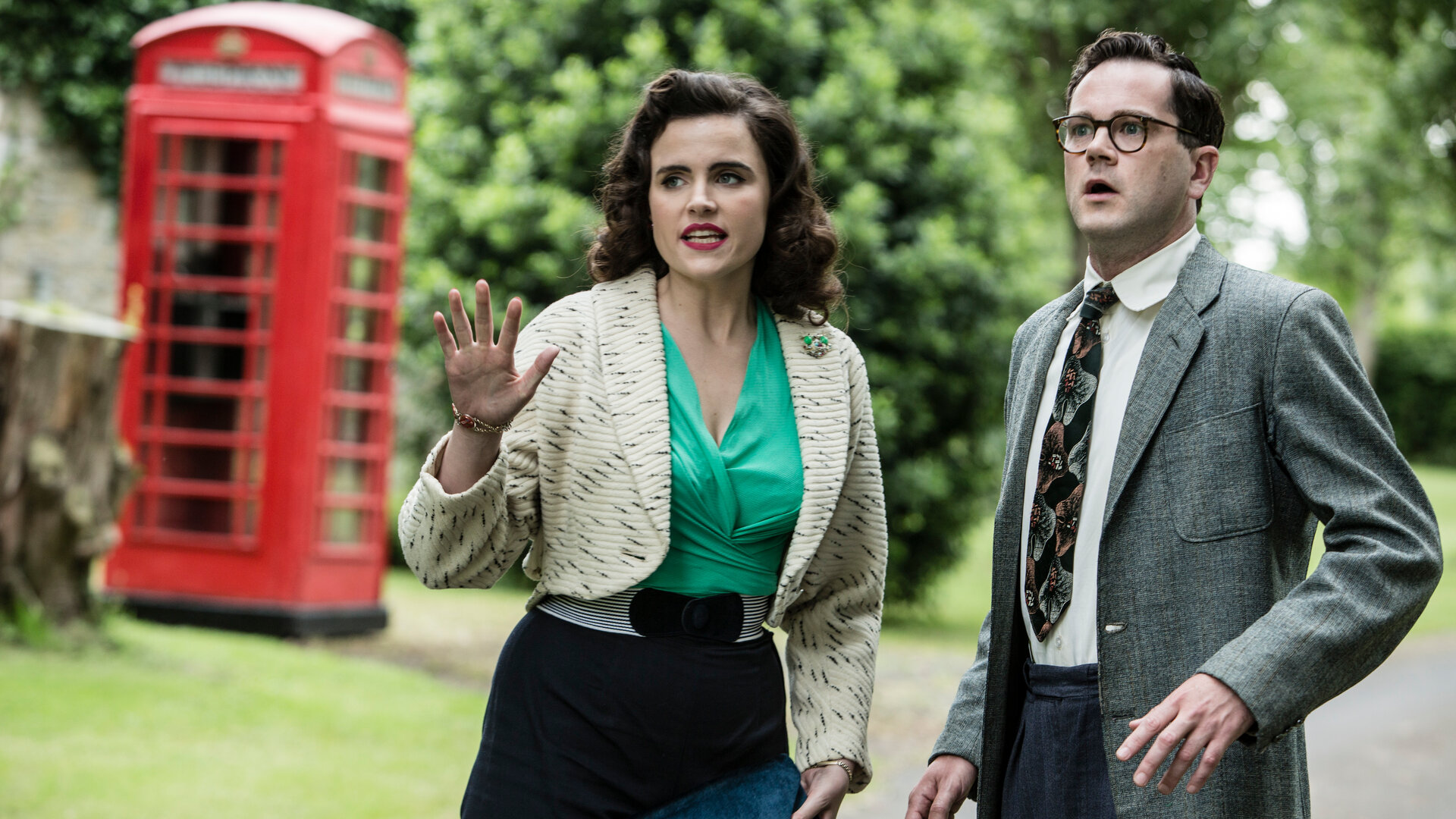 "Father Brown - Amors Pfeile": Bunty (Emer Kenny) und Jeremy Mayhew-Bowman (Simon Bubb) stehen nebeneinander und schauen schockiert in die gleiche Richtung. Im Hintergrund ist eine englische Telefonzelle zu erkennen.