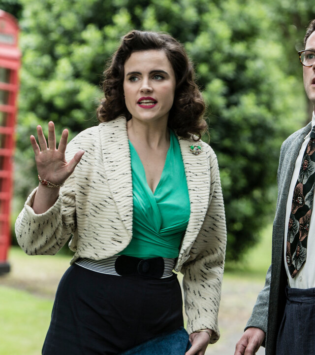 "Father Brown - Amors Pfeile": Bunty (Emer Kenny) und Jeremy Mayhew-Bowman (Simon Bubb) stehen nebeneinander und schauen schockiert in die gleiche Richtung. Im Hintergrund ist eine englische Telefonzelle zu erkennen.