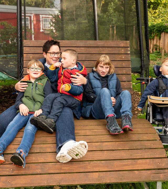 "einfach Mensch: Familie statt im Heim": Kerstin Held sitzt mit ihren vier Pflegekindern auf einer großen Gartenbank im heimischen Garten. Von links nach rechts: Maximilian, Kerstin Held, Richard, Cora und Jonathan.
