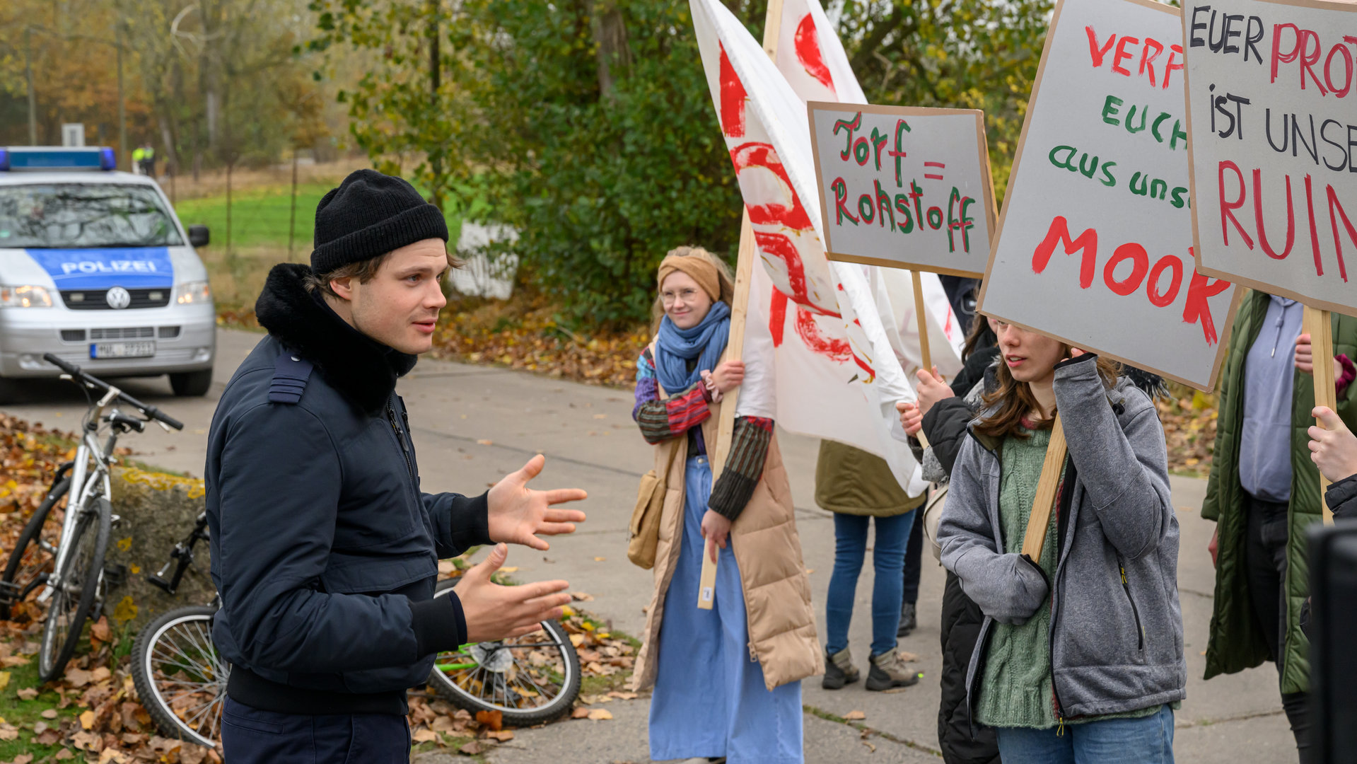 "SOKO Wismar – Tödlicher Torf": Eddi Jansons (Gustavs Gailus) steht gegenüber einer Gruppe von Demonstranten (Komparsen) und versucht beruhigend auf die diese einzuwirken.