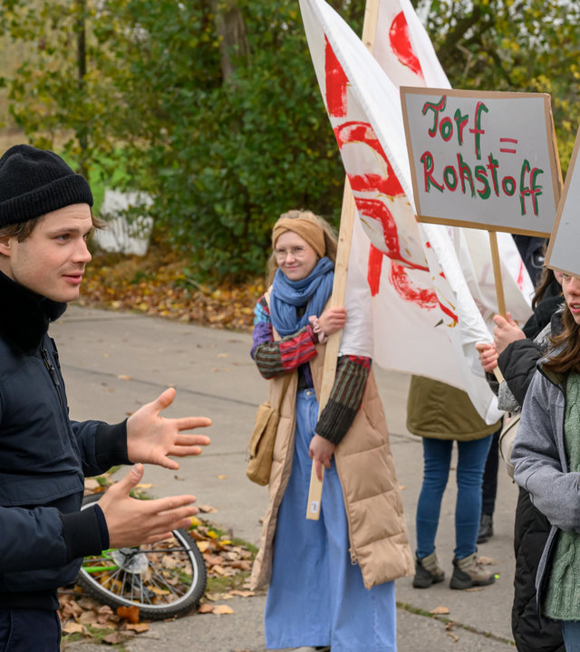 "SOKO Wismar – Tödlicher Torf": Eddi Jansons (Gustavs Gailus) steht gegenüber einer Gruppe von Demonstranten (Komparsen) und versucht beruhigend auf die diese einzuwirken.