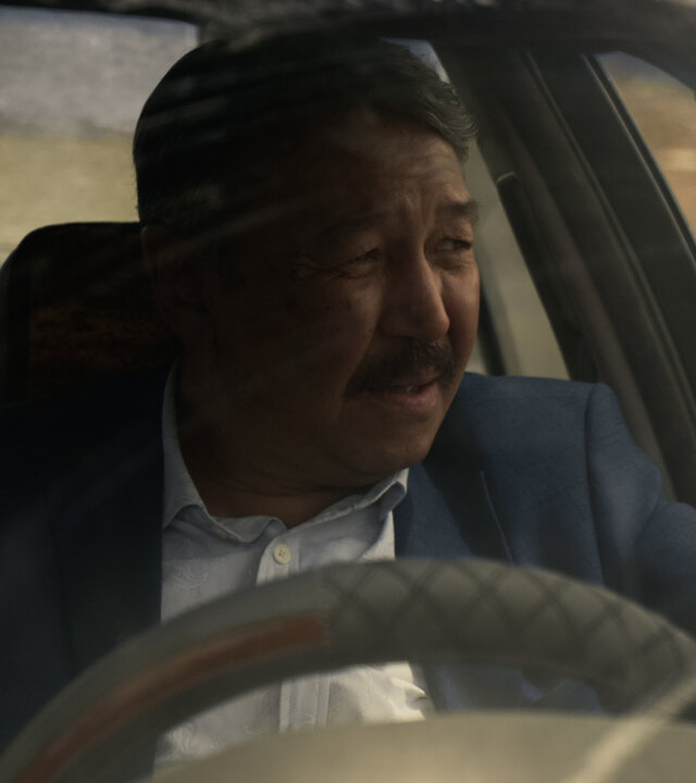 "Infiniti - Auf der anderen Seite des Spiegels": Askarev (Erken Gubashev) sitzt in einem Auto und schaut angespannt aus dem Fenster.