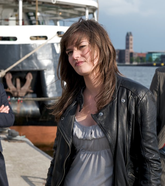 "SOKO Wismar - Der blonde Hans": Cindy Lundt (Diane Willems) steht mit dem Rücken zu den Ermittlern Katrin Börensen (Claudia Schmutzler) und Sven Herzog (Michael Härle) im Hafen von Wismar. Im Hintergrund ist ein Schiff vertäut, und die Stadt sowie der Hafen sind zu erkennen.