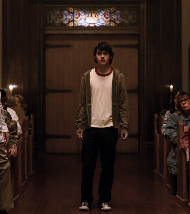 "Hysteria! - Die Nacht der Erlösung": Dylan (Emjay Anthony) steht allein im Mittelgang einer vollbesetzten Kirche, umgeben von Menschen (Komparsen), die ihn aufmerksam ansehen.