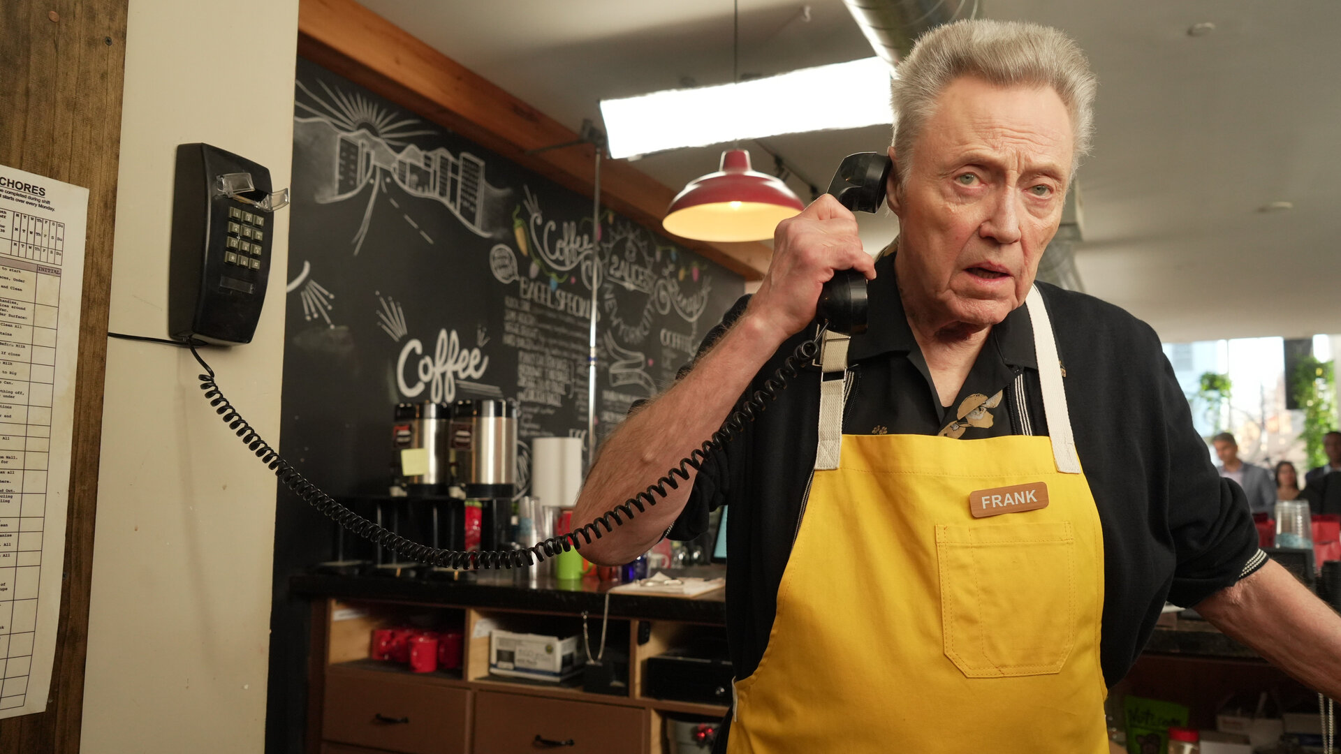 "The Outlaws - Moral war gestern": Frank (Christopher Walken) steht mit einer gelben Schürze bekleidet in einem Café und hält einen Telefonhörer an sein Ohr.