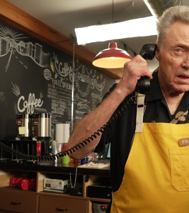 "The Outlaws - Moral war gestern": Frank (Christopher Walken) steht mit einer gelben Schürze bekleidet in einem Café und hält einen Telefonhörer an sein Ohr.