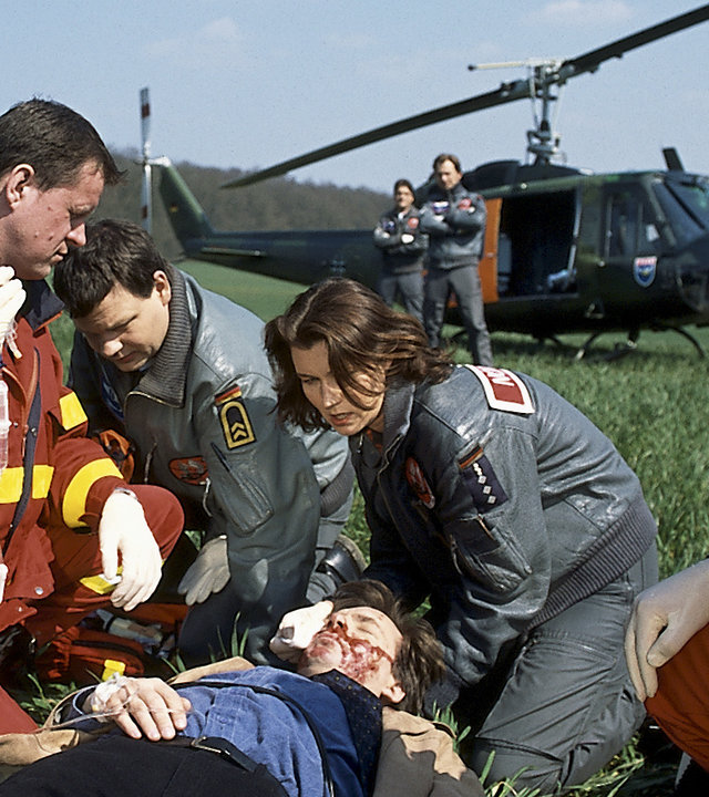 "Die Rettungsflieger - Wollckes Wagnis": Slawomir (Tomek Nowicki) liegt schwer verletzt auf einer Wiese. Ilona (Julia Heinemann) und Thomas (Ulrich Bähnk) knien zusammen mit zwei Sanitätern neben ihm und versorgen ihn. Im Hintergrund sieht man zwei weitere Rettungsflieger und den Hubschrauber.