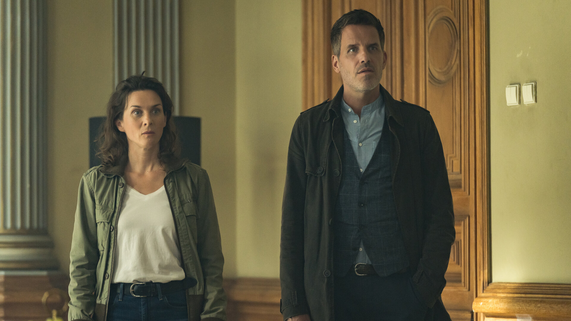 "In ewiger Freundschaft (1) - Ein Taunuskrimi": Mit offenen Blicken steht Pia Sander (Kathrin von Steinburg) neben ihrem Kollegen Oliver von Bodenstein (Tim Bergmann) in einem Raum mit antiken Säulen vor einer hohen, aufwendig gestalteten Holztür.