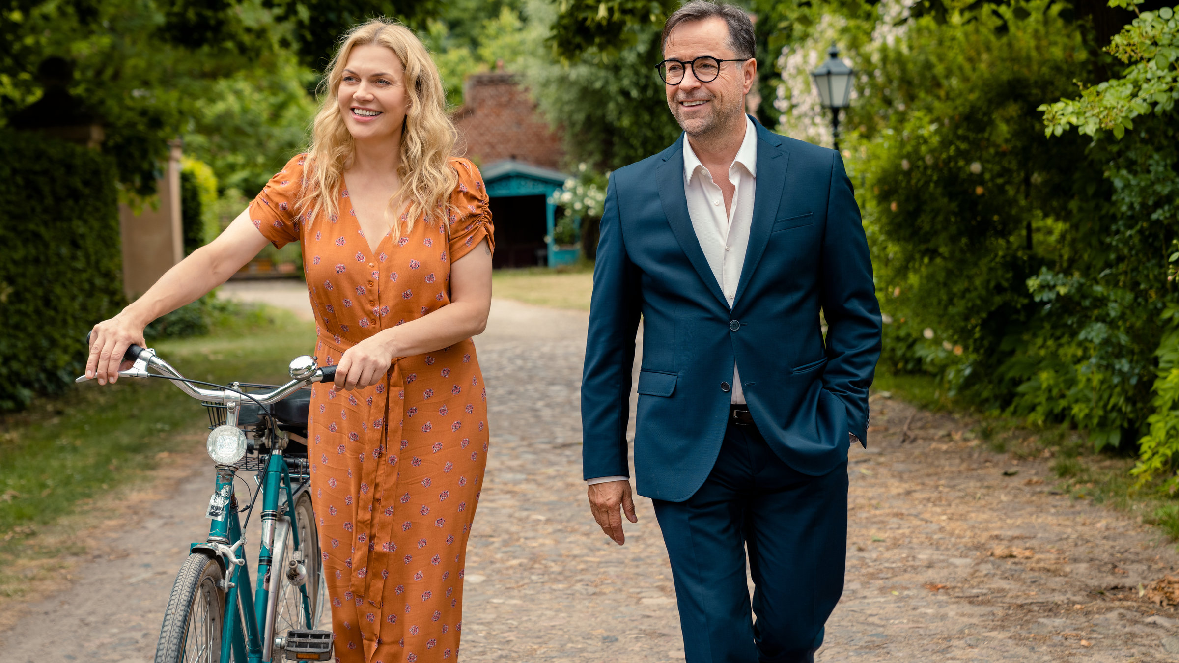 "Düstersee": Sanja Huth (Anna Loos) schiebt ihr Fahrrad auf einem Weg. Joachim Vernau (Jan Josef Liefers) läuft nebenher.