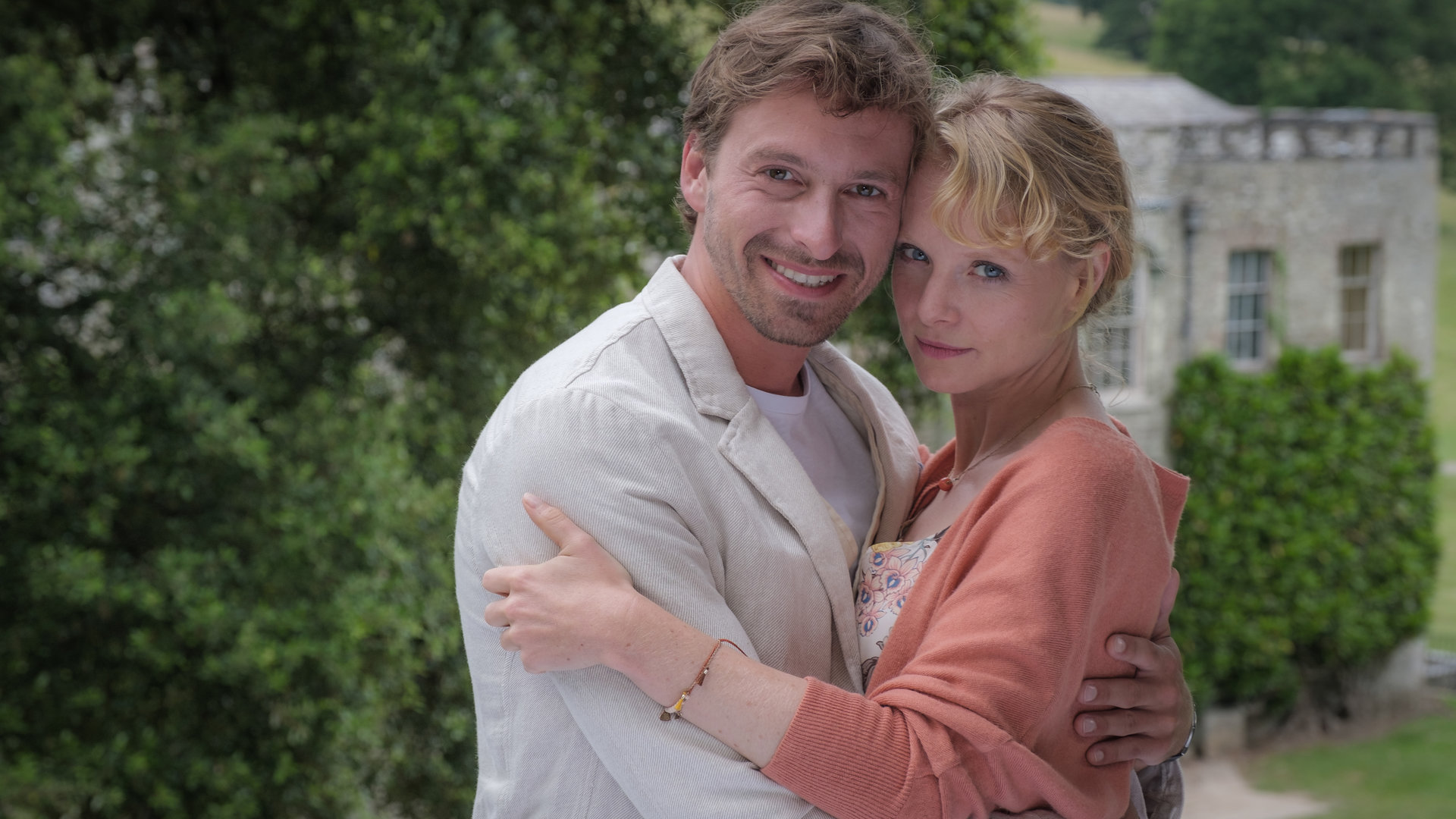 "Rosamunde Pilcher: Wenn Fische lächeln": Ray (Ben Blaskovic) und Liz (Friederike Ott) stehen Arm in Arm vor einem großen Anwesen und lächeln in die Kamera.
