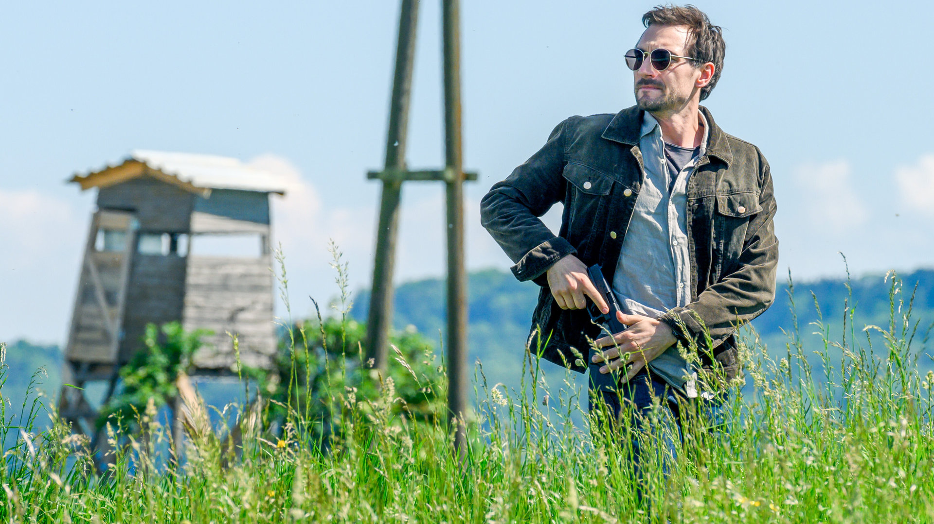 "SOKO Linz- Tödliche Ernte": Ben Halberg (Daniel Gawlowski) steht mit Sonnenbrille und gezückter Waffe in einem Feld. Er blickt sich suchend um.