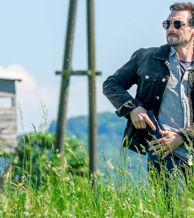 "SOKO Linz- Tödliche Ernte": Ben Halberg (Daniel Gawlowski) steht mit Sonnenbrille und gezückter Waffe in einem Feld. Er blickt sich suchend um.