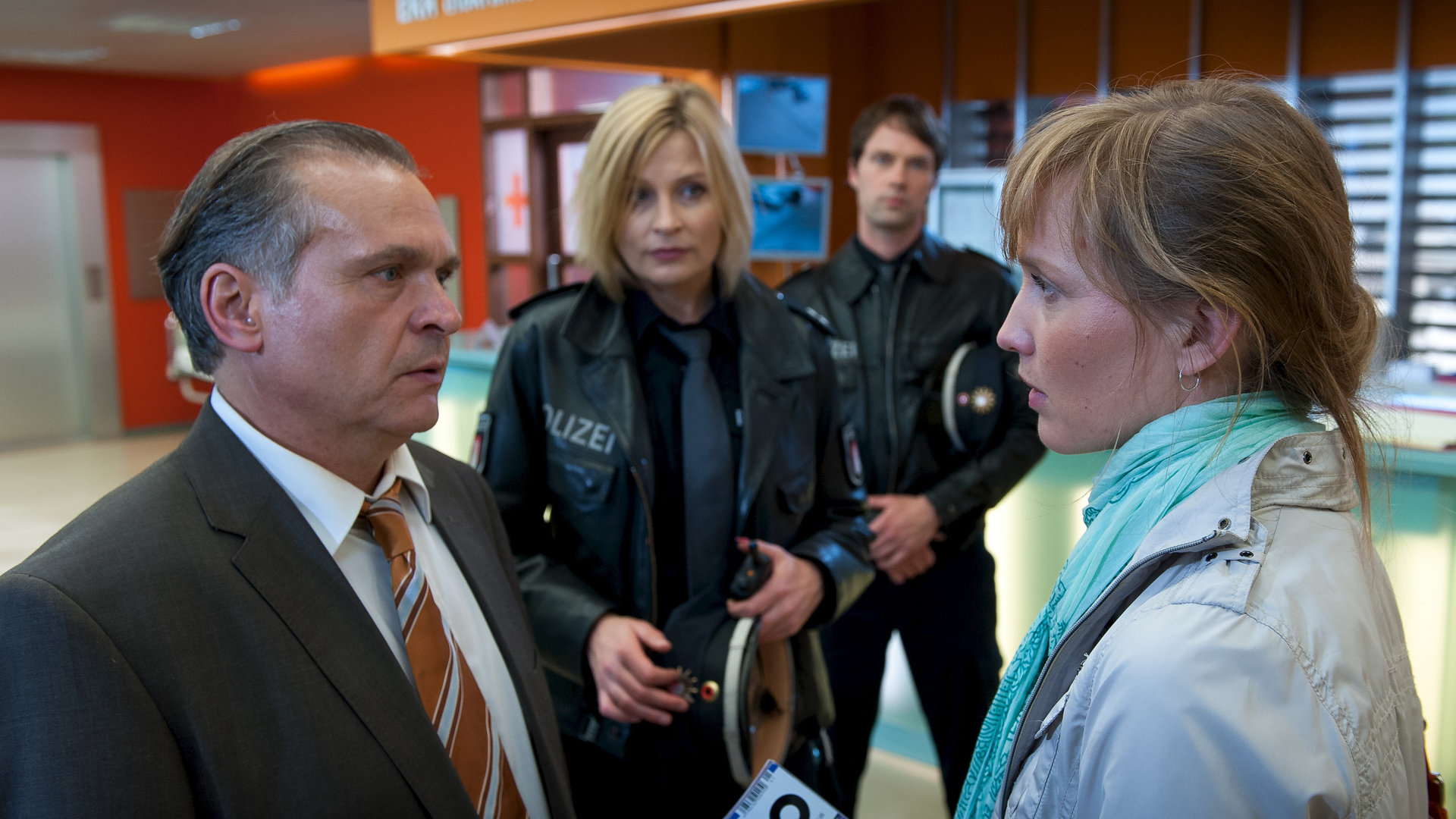 "Notruf Hafenkante - Schuss ins Herz": Melanie (Sanna Englund) und Mattes (Matthias Schloo) stehen auf dem Krankenhausflur und beobachten ein Gespräch zwischen Susanne (Verena Wolfien) und ihrem Vater Carl (Jockel Tschiersch).