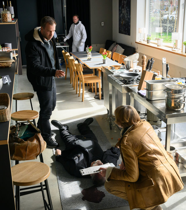 "SOKO Wismar - Haukes Dinner": Dr. Helene Sturbeck (Katharina Blaschke) kniet in der Küche vor dem toten Hauke Kahnemann (Marcus Kaloff). Lars Pöhlmann (Dominic Boeer) hat einige Fragen an sie.