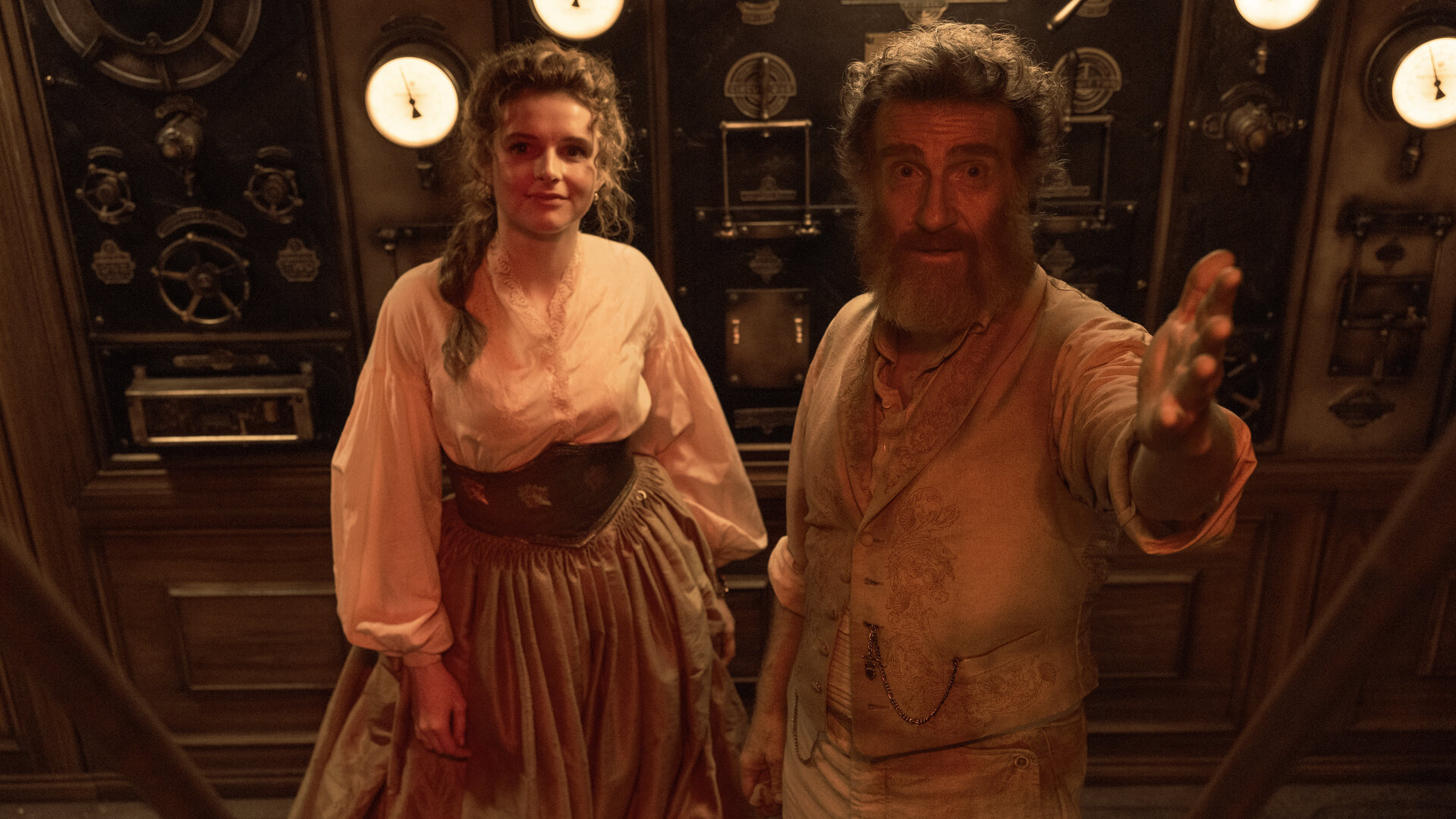 "Nautilus - Gejagt": Humility (Georgia Flood) und Benoit (Thierry Frémont) stehen nebeneinander in einem Raum. Hinter ihnen stehen technische Geräte. Er hebt seine linke Hand und deutet auf etwas.