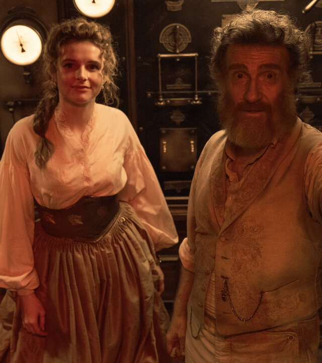 "Nautilus - Gejagt": Humility (Georgia Flood) und Benoit (Thierry Frémont) stehen nebeneinander in einem Raum. Hinter ihnen stehen technische Geräte. Er hebt seine linke Hand und deutet auf etwas.