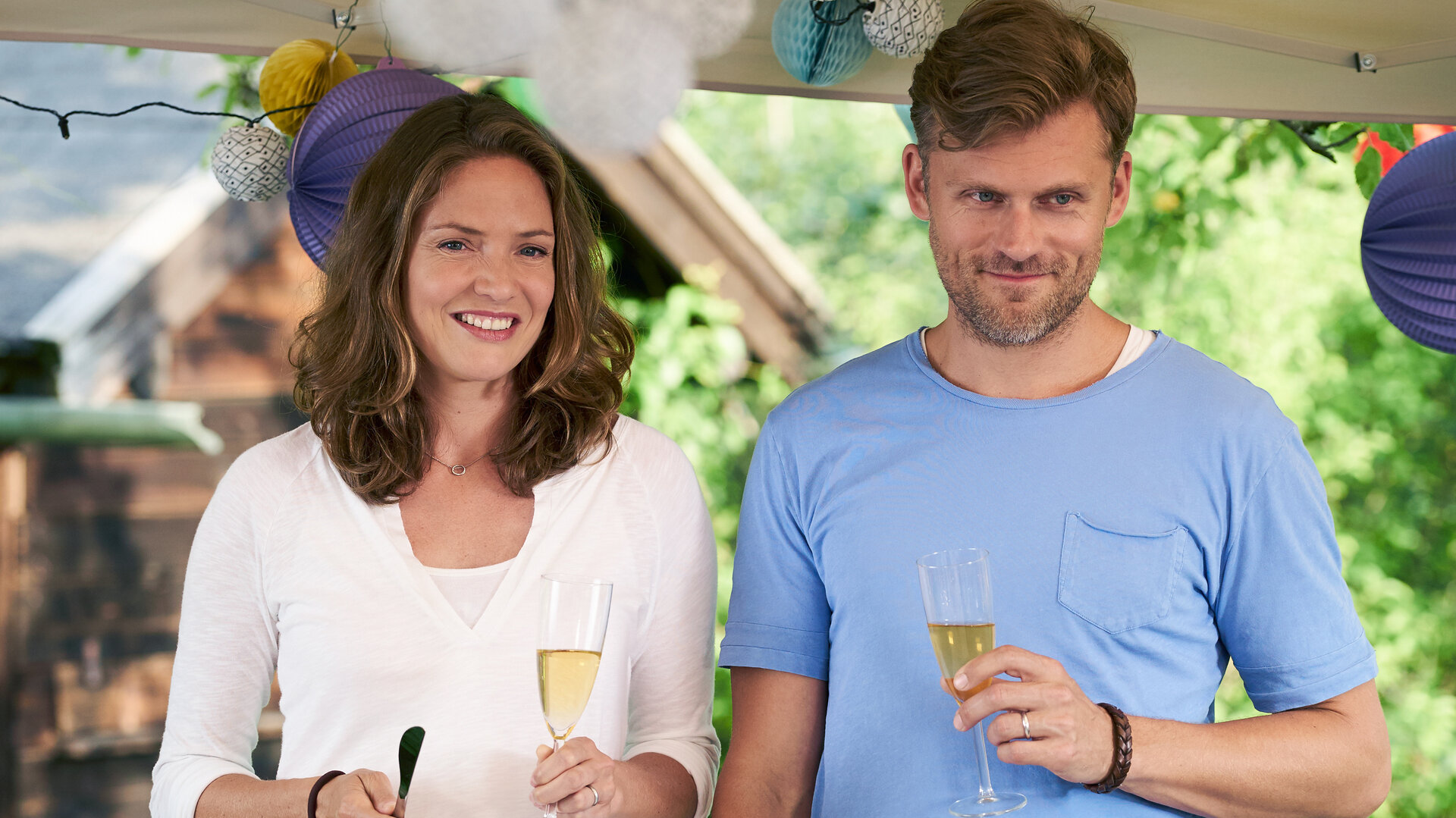 "Lena Lorenz - Babyglück hoch drei (2)": Lena (Patricia Aulitzky) und Quirin (Jens Atzorn) stehen mit Sektgläsern in den Händen unter einem offenen Zeltdach.