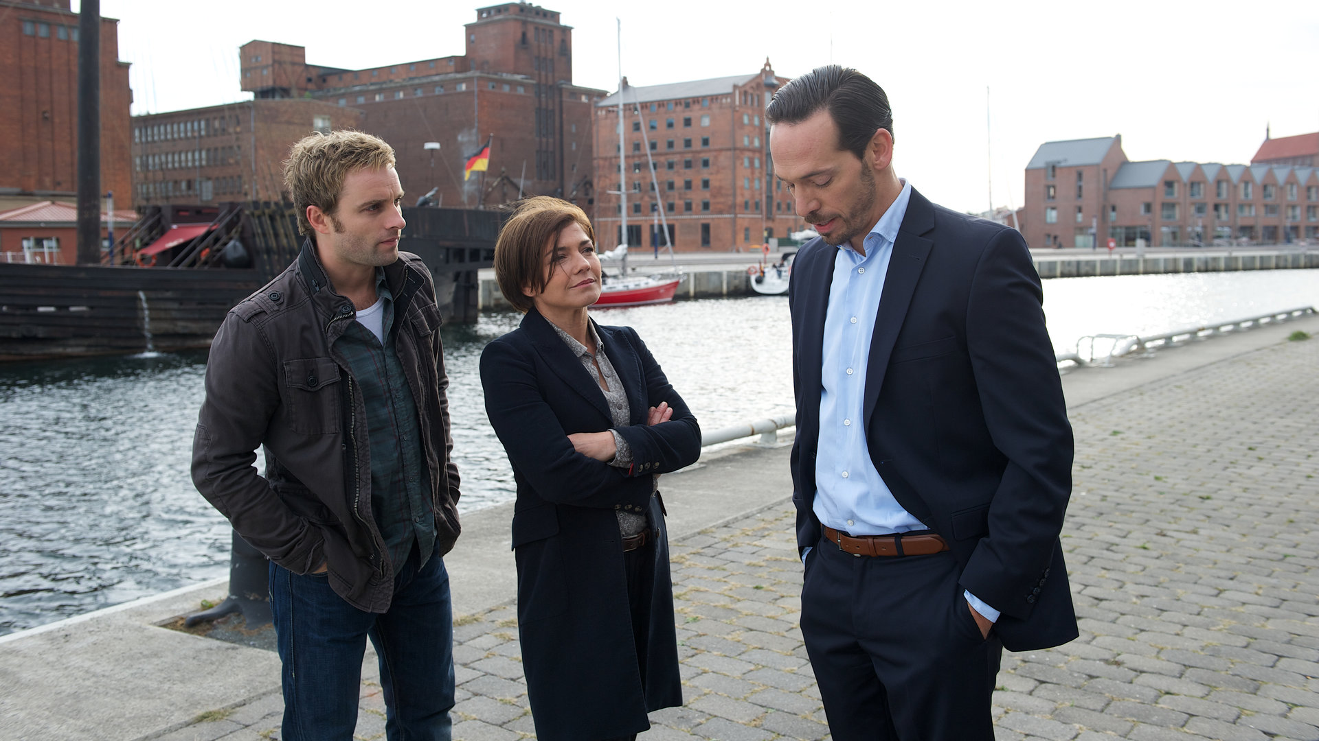 "SOKO Wismar - Der Stachel in mir": Nils Theede (Jonas Laux) und Katrin Börensen (Claudia Schmutzler) stehen am Hafen und hören zu, was Ralf Mitzerlich (Markus Klauk) ihnen zu berichten hat. Ralfs Blick ist auf den Boden gerichtet, die Hände hat er in den Hosentaschen.