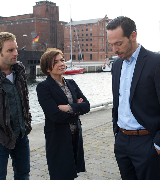 "SOKO Wismar - Der Stachel in mir": Nils Theede (Jonas Laux) und Katrin Börensen (Claudia Schmutzler) stehen am Hafen und hören zu, was Ralf Mitzerlich (Markus Klauk) ihnen zu berichten hat. Ralfs Blick ist auf den Boden gerichtet, die Hände hat er in den Hosentaschen.