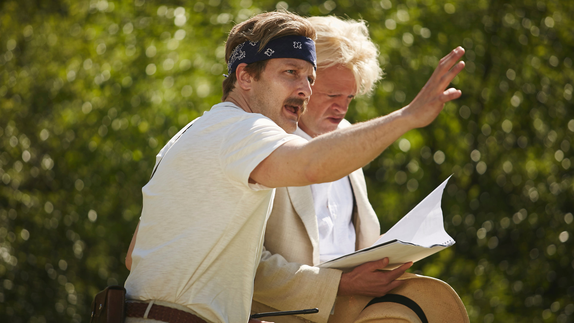 "Sketch History – Neues von gestern": Klaus Kinski (Max Giermann) blättert skeptisch blickend in seinem Drehbuch, während ihm Werner Herzog (Holger Stockhaus) mit ausgestrecktem Arm, und ein Bandana tragend, Anweisungen gibt. Beide stehen in einem Außenset eines Filmdrehs und sind hell bekleidet.