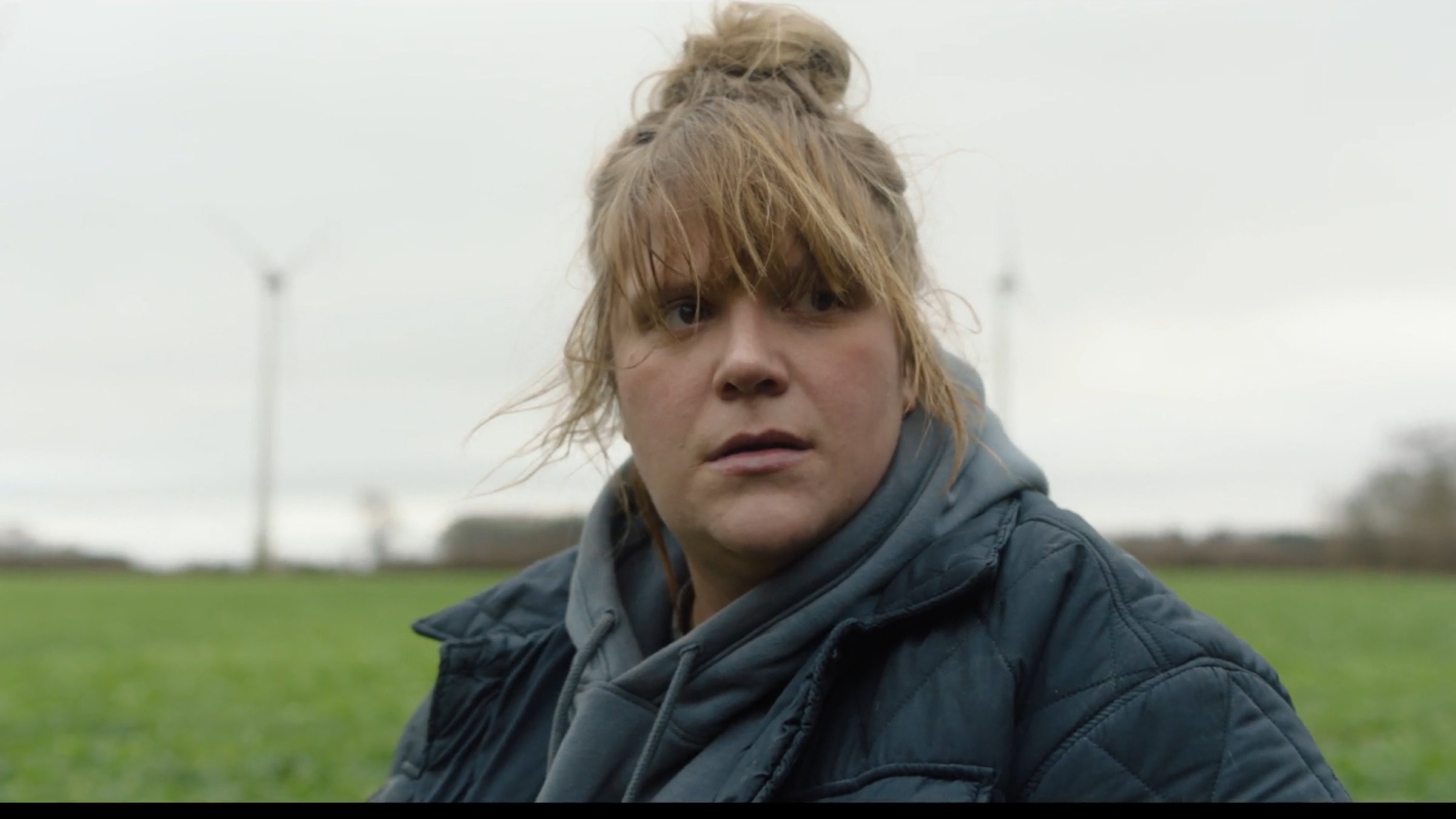 „KlassiXS – die großen Dramen in jungen Kurzfilmen: Kalb“: Franziska (Stefanie Reinsperger) mit zerzauster Frisur und warmer Jacke auf einer Wiese. Sie sieht nicht sehr glücklich aus.