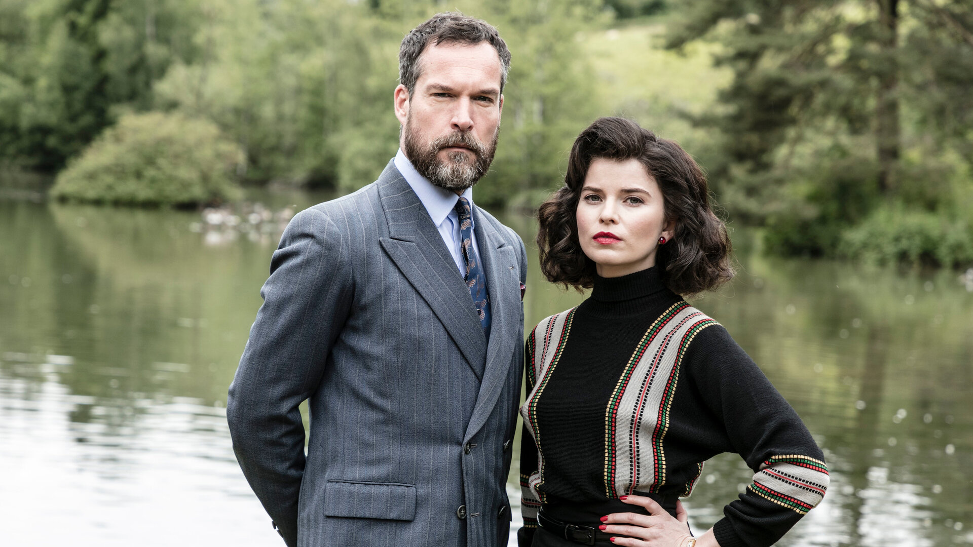 "Father Brown - Der Familienwettstreit": Die Konkurrenten Hercule Flambeau (John Light) und Marianne Delacroix (Gina Bramhill) stehen am See.