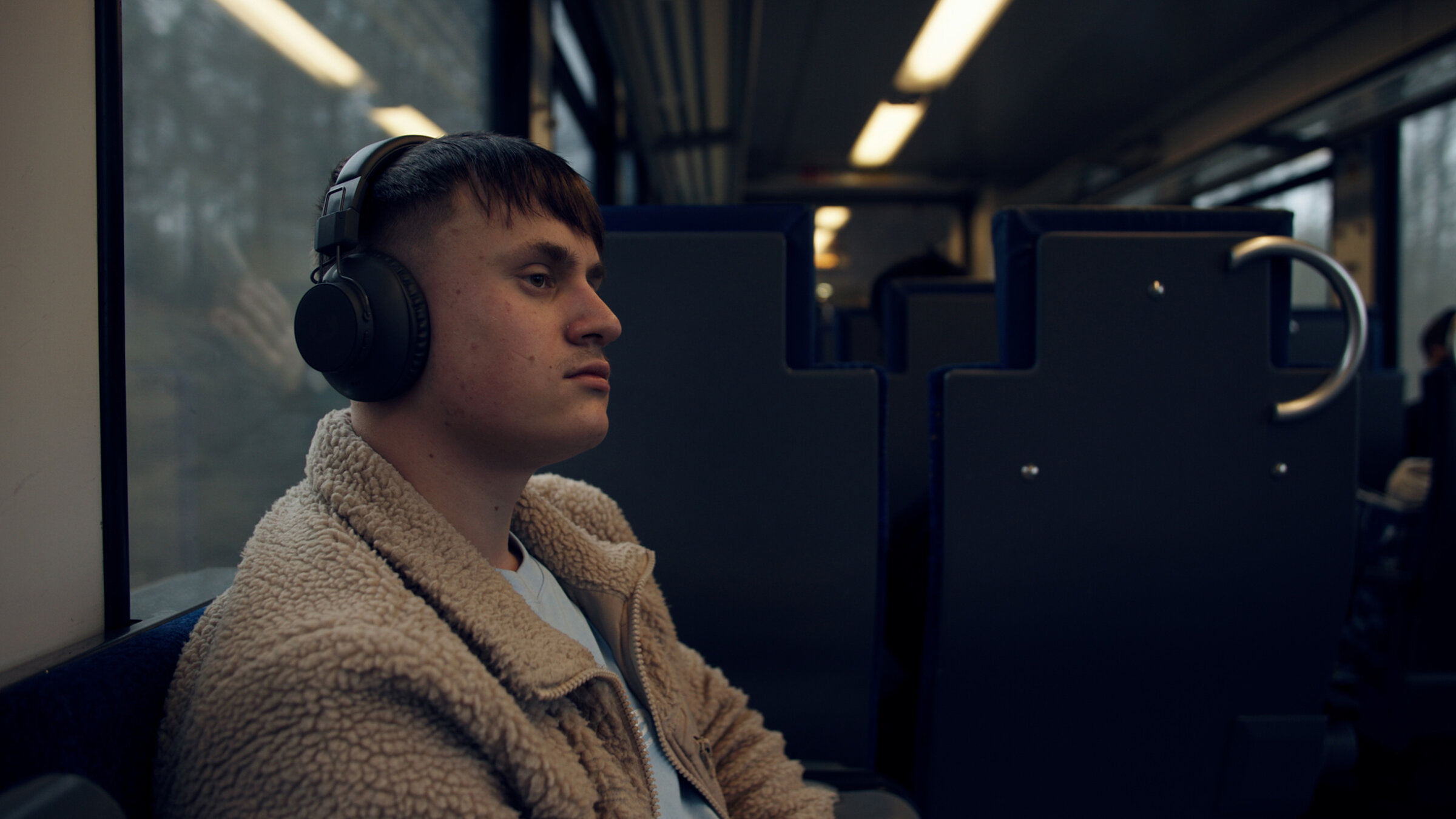 "DocuMe - Nikolai": Junger Mann mit Kopfhörern sitzt in einem Zug am Fenster.