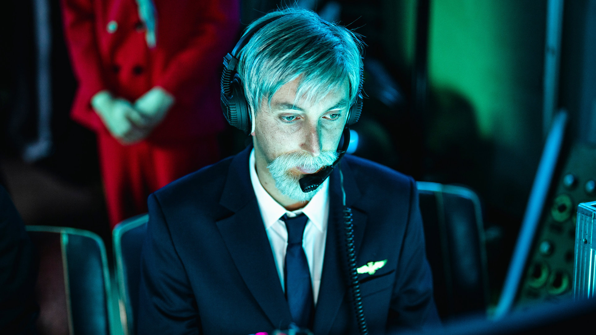 "Einsame Herzen - Folge 6": Roger (Torge Oelrich) sitzt in einer Pilotenuniform und einem Headset am Computer.