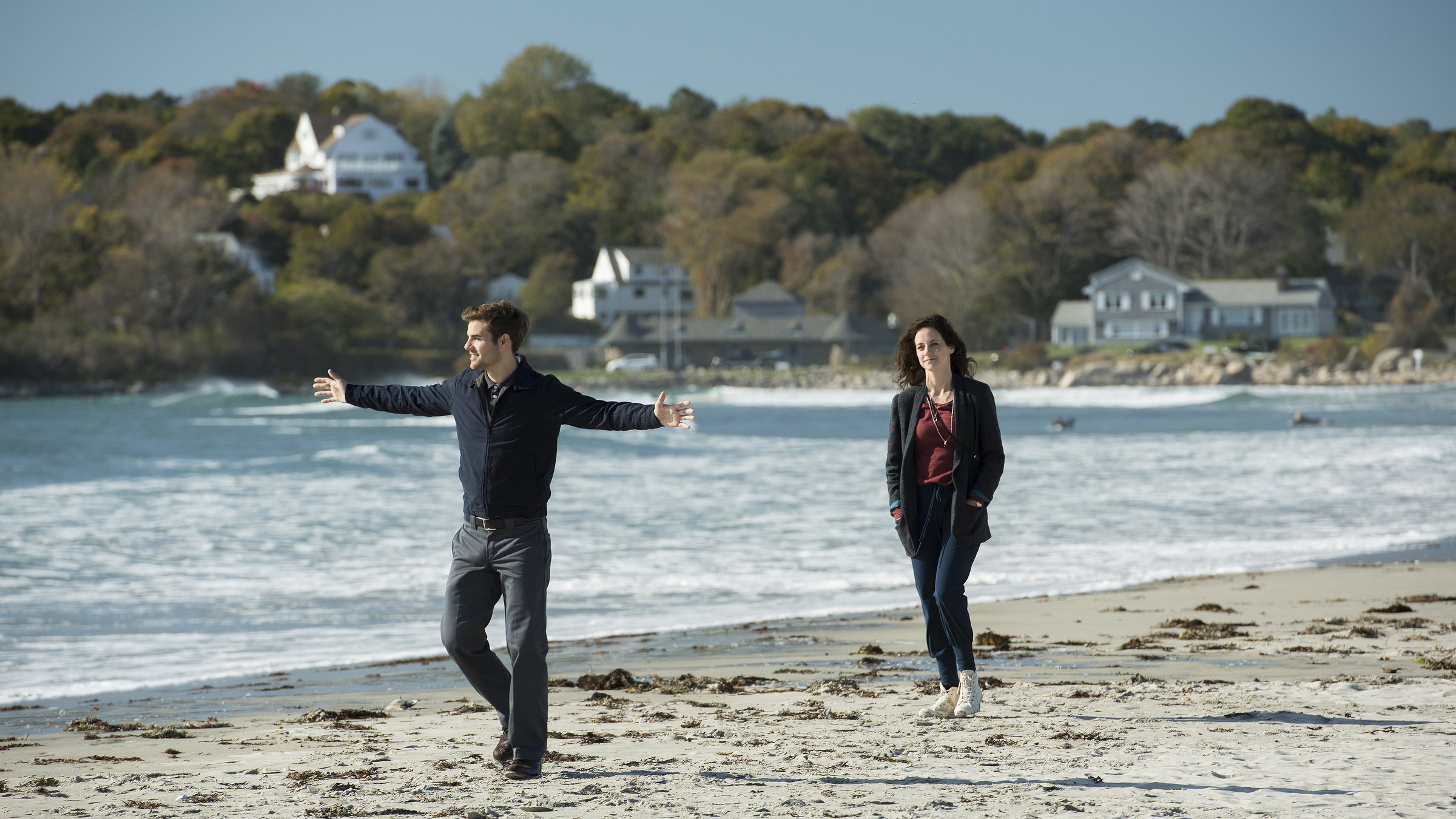 "Katie Fforde: Bruderherz": Das ungleiche Geschwisterpaar Lauren (Anja Knauer) und Anthony Cahill (Lucas Reiber) macht gemeinsam einen Strandspaziergang. Anthony geht voraus und hat die Arme ausgebreitet.