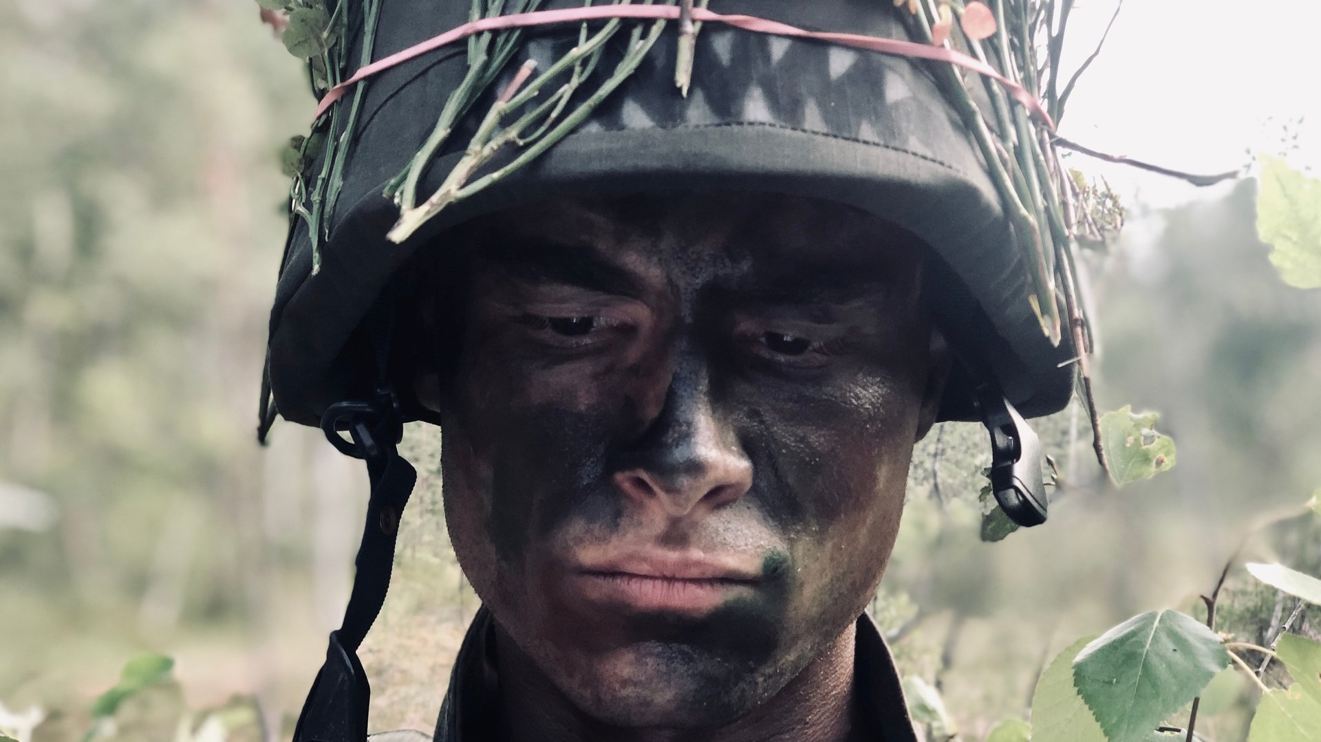 "Californian Commando - Camping": Van (Kian Lawley) steht mit dunkler Gesichtsbemalung und Ästen zur Tarnung im Wald und schaut bedrückt nach unten.