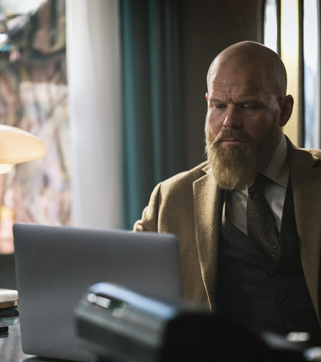 "Toxic Tom - Das Ende von Tom": Der Modeverkäufer Tom Hallsténsen (Anders Baasmo) sitzt am Tresen seiner Damenboutique und blickt auf einen aufgeklappten Laptop.