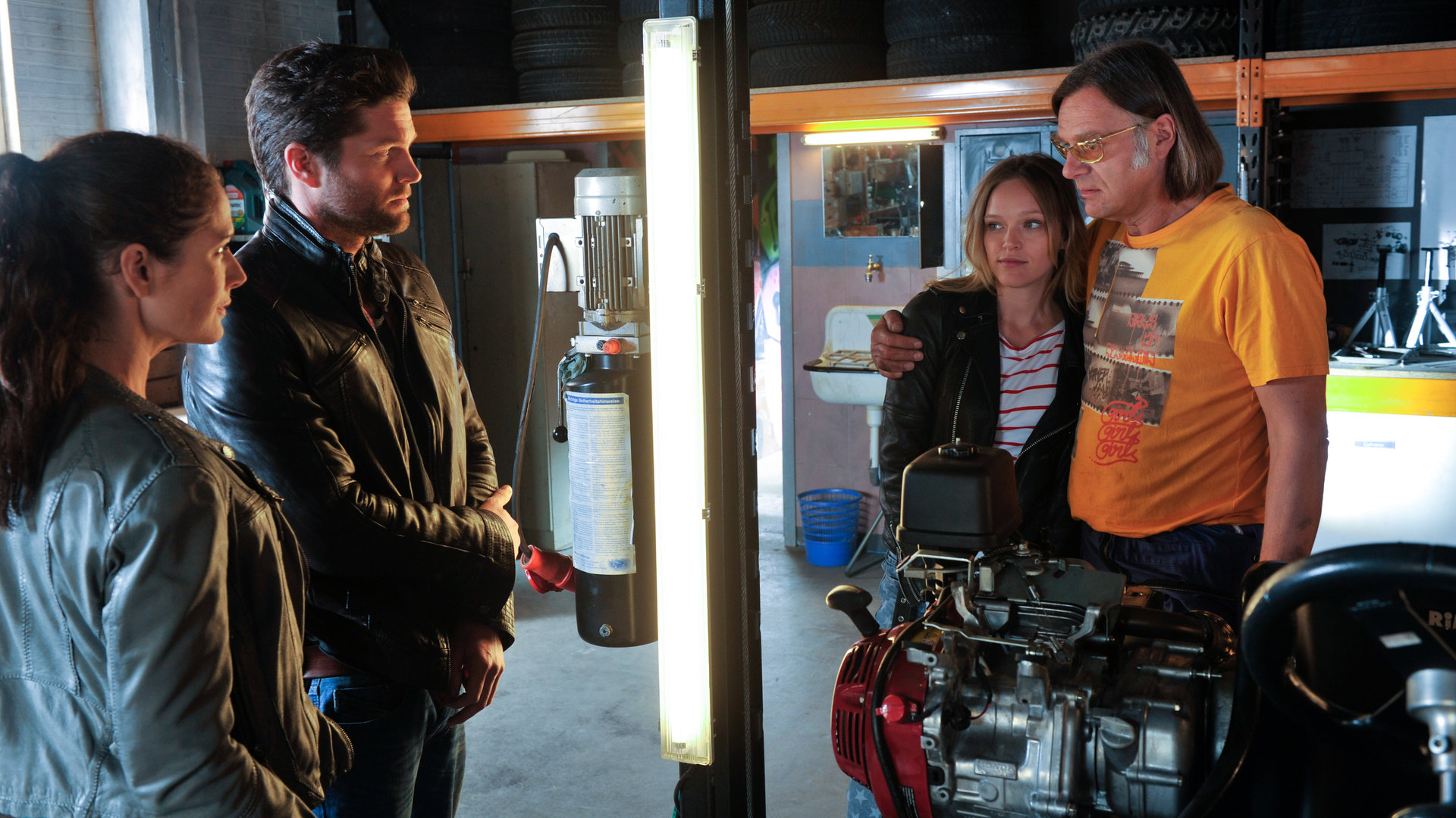 "SOKO Stuttgart - Ausgebremst": Selma Kirsch (Yve Burbach) und Jo Stoll (Peter Ketnath) stehen in "Schrottis" Werkstatt. Sie schauen zu Karl-Heinz "Schrotti" Schrothmann (Michael Gaedt), der seinen Arm um seine Patentochter Hannah Weinmeier (Livia Matthes) gelegt hat.