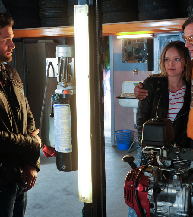 "SOKO Stuttgart - Ausgebremst": Selma Kirsch (Yve Burbach) und Jo Stoll (Peter Ketnath) stehen in "Schrottis" Werkstatt. Sie schauen zu Karl-Heinz "Schrotti" Schrothmann (Michael Gaedt), der seinen Arm um seine Patentochter Hannah Weinmeier (Livia Matthes) gelegt hat.