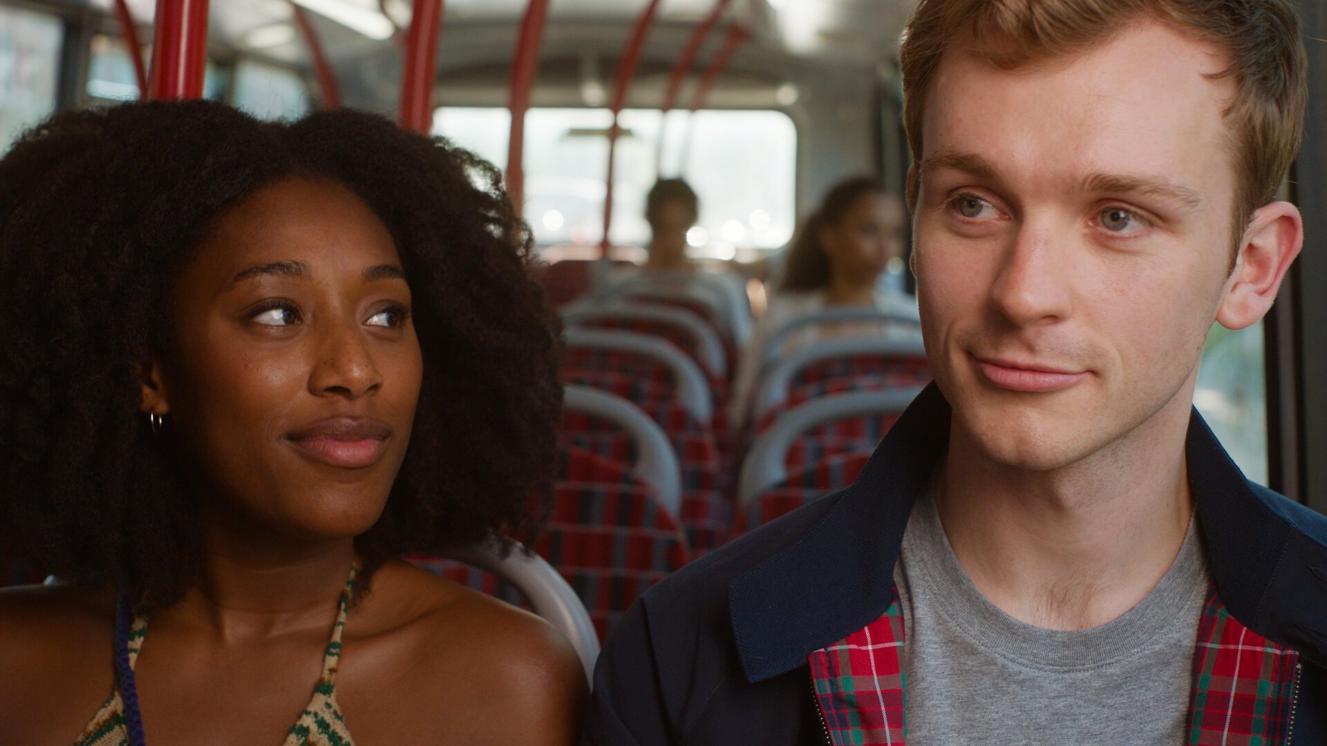 "You & Me": Jess (Sophia Brown) und Ben (Harry Lawtey) sitzen lächelnd nebeneinander im Bus, während Jess ihn von der Seite betrachtet.