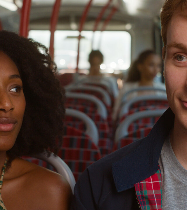 "You & Me": Jess (Sophia Brown) und Ben (Harry Lawtey) sitzen lächelnd nebeneinander im Bus, während Jess ihn von der Seite betrachtet.