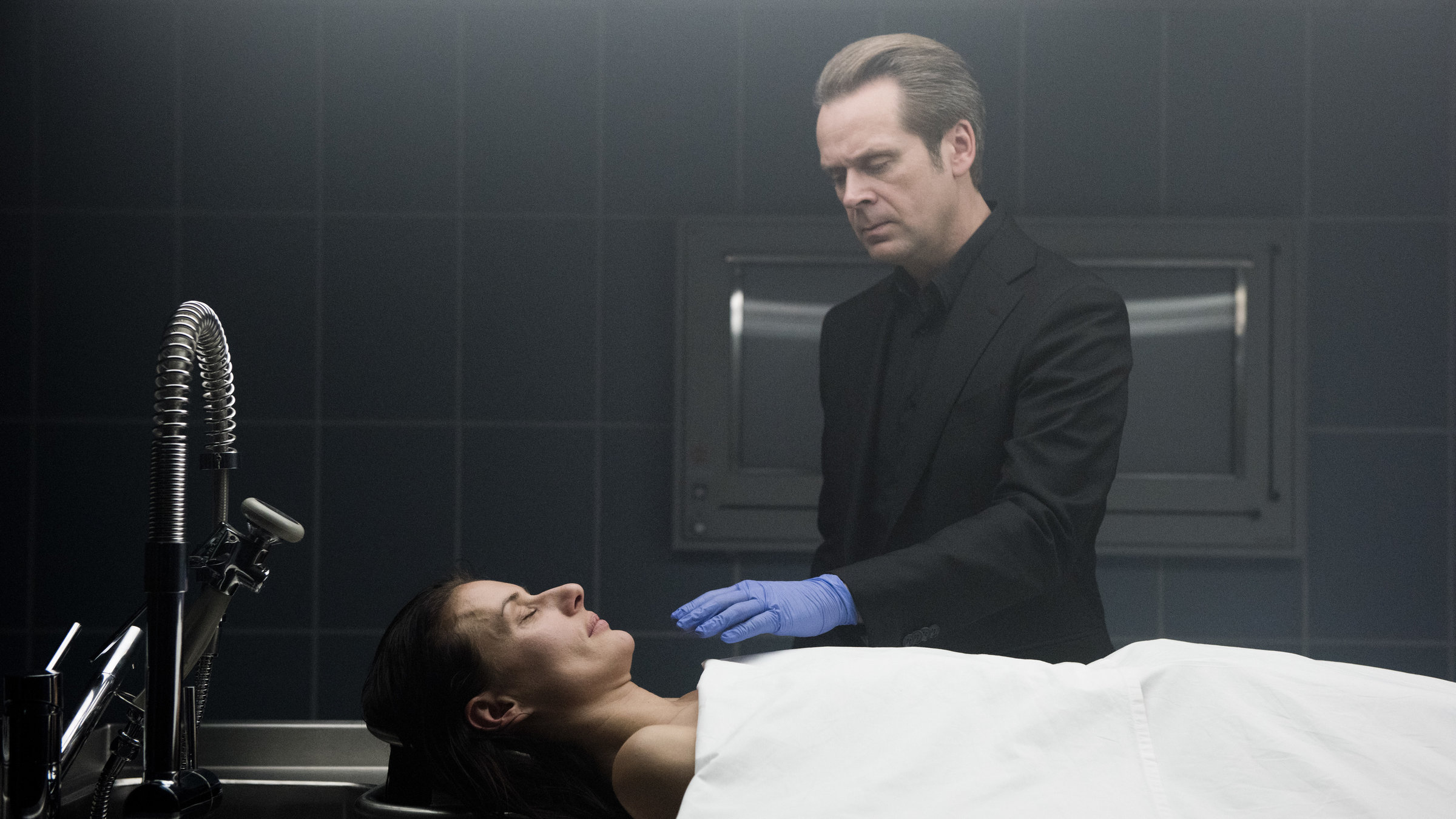 "Professor T. - Tamara": Professor T. (Matthias Matschke) steht im Leichenschauhaus vor der toten Tamara Frings (Marie Rönnebeck). Er trägt einen Handschuh und greift nach ihrem Gesicht.